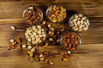 Assortment of nuts on wooden table. Almond, hazelnut, pistachio, walnut and cashew in glass bowls. Top view. Healthy eating concept