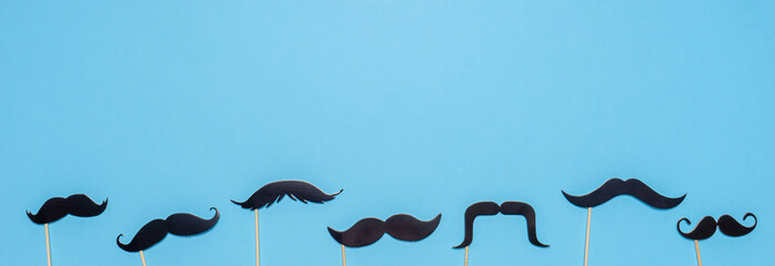 Various black photo booth props moustaches of different shape on blue background. Greeting card for...