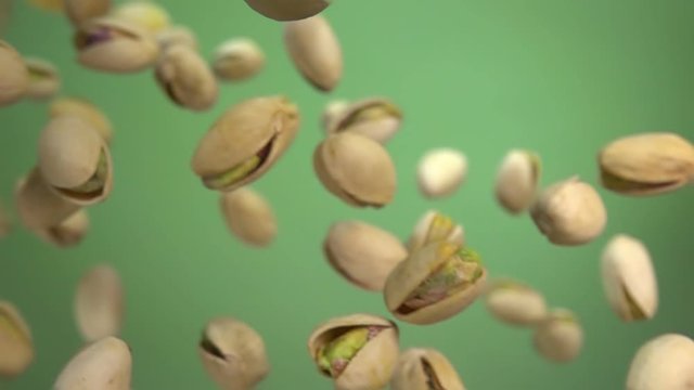 Close up of salted pistachios flying diagonally on green background in slow motion