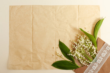 Vintage background with fresh white flowers. Beautiful garden lilies of the valley with leaves in a waffle cone and envelope. Empty craft paper background in the center for text, top view