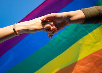 hands of a lesbian couple outdoors. LGBT rainbow flag.