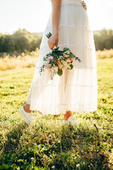 Bride at sunset holding a wedding bouquet in her hands.