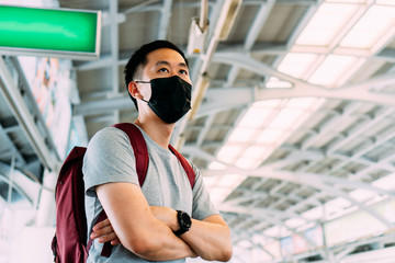 Close up of one young Asian man wearing a black surgical face mask waiting for the train during new type Coronavirus Covid-19 pneumonia outbreak and pm 2.5 smog air pollution crisis in big city.