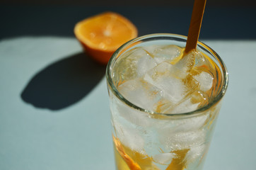 lemon refreshing water with ice in a glass glass with a yellow tube against the background of half a lemon