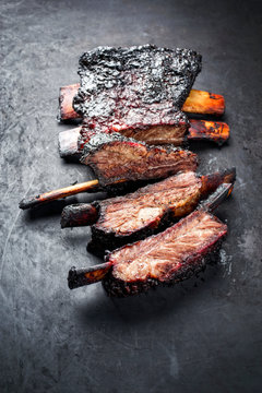 Barbecue burnt chuck beef ribs marinated with hot chili sauce as closeup on an old rustic board