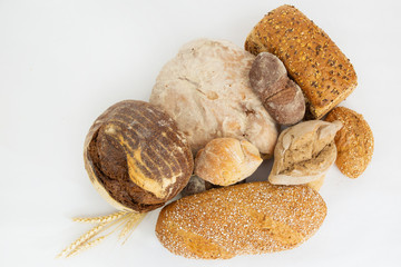 Wheat and rye pastry with cereals or seeds and ears of wheat. Delicious loafs and buns isolated on white background. Studio shot. Top view. Homemade food and nutrition concept