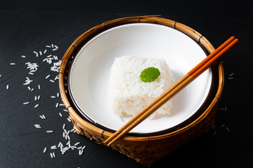 Asian Food concept cooked Thail jasmine rice long grain rice in ceramic bowl and bamboo tray on black slate board background with copy space