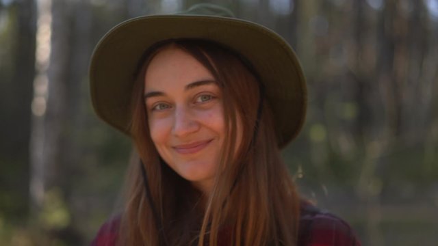 close-up portrait joyful shy young  hipster female in forest smiling looking at camera. Beautiful millennial woman in hat, hiking equipment enjoy camping day  nature, adventure freedom concept