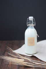 Glass bottle of milk on dark rustic wooden table. Ears on first plan. written MILK. Black background