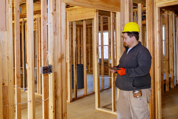 Inspector with yellow hard hat checking electrical wiring inside house