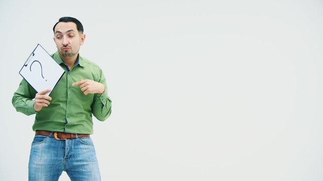 Funny dancing young man holding a paper holder with writen on it question mark, pointing his finger at this mark.