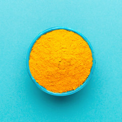 Top view turmeric powder in blue bowl at orange background.