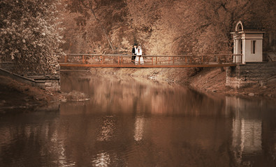 A pair of men in a black tailcoat and hat and a woman in a beige hat, in a white dress, with a lace...