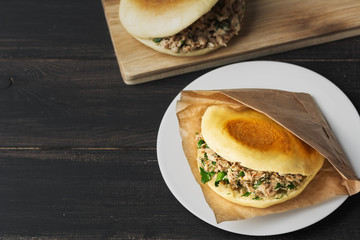 Rou jia mo Chinese hamburger is a popular street food. Pictured is a homemade sandwich in a white plate on a black wooden table. Top view. Copy space. Flat lay.