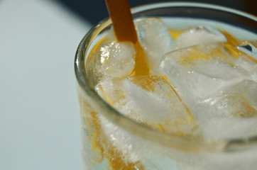 ice in a glass glass with lemonade and a yellow paper tube close-up