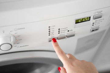 The girl sets the washing program for the washing machine.