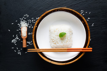 Asian Food concept cooked Thail jasmine rice long grain rice in ceramic bowl and bamboo tray on black slate board background with copy space