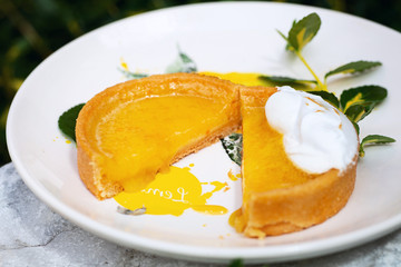 Cut citrus tartlet on the white plate decorated with painted lemon and white flower on it