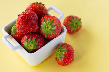  red fresh strawberry berries in white ceramic dishes on a colored background, copyspace