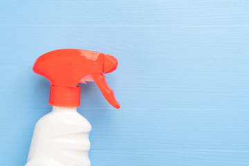Bottle of cleaning spray with a white case without inscriptions and a red bright dispenser on a wooden light blue background