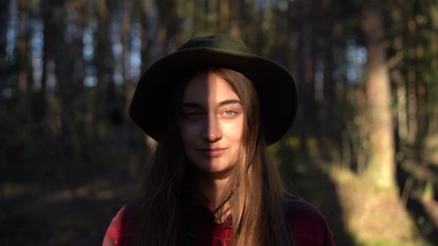close up portrait of young attractive caucasian hipster female farmer worker green eyes long hair, forest nature adventure concept. millennial girl in hat and checked shirt look straight at camera