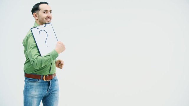 Funny young man dancing with holding a paper holder with writen on it question mark, watching surprisingly at at this mark and pointing his finger.