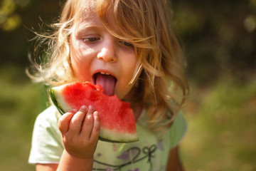cute fun little girl eating a piece of watermelon in the garden in summertime