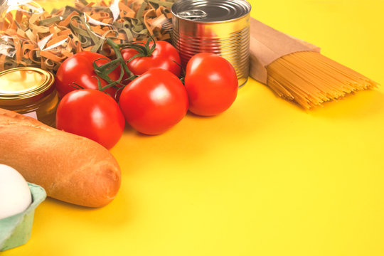 Close up of donation food on yellow background with copyspace - pasta, fresh vegatables, canned food. Donation or delivery food concept