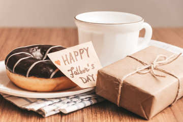 Gift box with a tag, cup of coffee or tea and chocolate donut. Father's day or birthday concept.