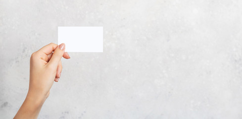 Female hand holding a blank business card, cutaway on gray concrete background with copy space. Branding mockup template. Mockup