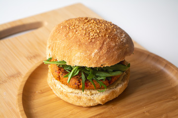 Vegan falafel hummus burger with homemade sourdough bun, tomatoes, pickled cucumbers and arugula in a wooden plate