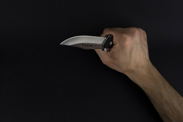 The man is holding a shiny and sharp hunter knife with his hand on the black background. Hunting,...