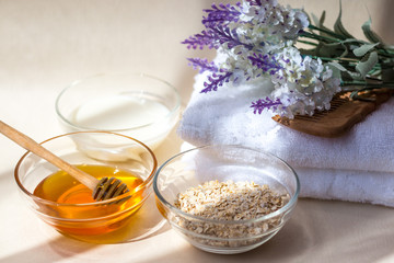Home Spa skin care ingredients. Glass jars of oatmeal and yellow honey, a white towel for the bathroom. There is a lavender flower in the background. Side view. Sunlight.