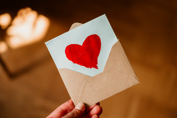 A person holding a love letter with a painted red heart on it in a brown envelope