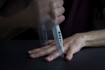 The man is playing a game with shiny and sharp hunter knife. He is striving to hitting the knife...