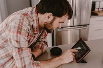 Young man millennial hipster orders food with tablet. Online food delivery. Ordering food online. Using app for delivery. Smart speaker. Smart home. Using modern technology at home. Making phone call