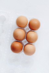 Brown chicken eggs in plastic container on white wooden background. Top view.