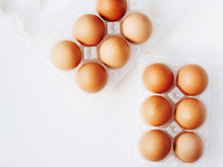Brown chicken eggs in plastic container on white wooden background. Top view.