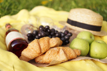 Picnic on the grass with croissant, pink wine, straw hat, grape on yellow plaid and green grass. Summer time