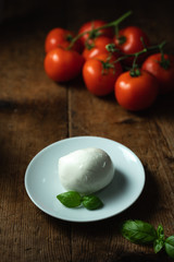 mozzarella on a plate with basil leaves and tomatoes on the background