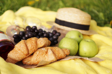 Picnic on the grass with croissant, pink wine, straw hat, grape on yellow plaid and green grass. Summer time