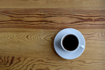 The white cup of coffee is on a wooden beige surface. Above view.