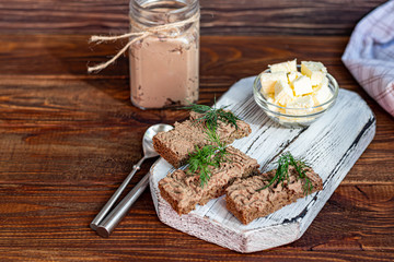 Fresh homemade chicken liver pate with carrots, onions and butter. Garnished with a sprig of dill. Lubricated on bread. On a wooden background.