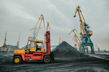 Heavy duty forklift truck parked near huge pile of coal. Dock distribution center