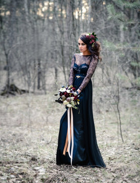 A Gothic woman in a black dress with a bouquet of flowers in a mysterious forest. Black magic, Gothic beauty, mystical image