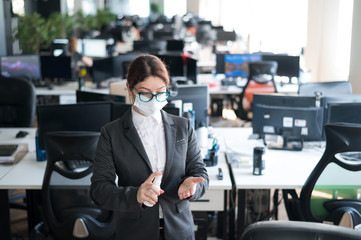 Fototapeta premium Female manager in a medical mask sprays on hand antiseptic. A woman in a suit uses a sanitizer to disinfect. Concept of office work during the coronavirus epidemic.