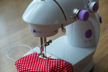 Face mask sewing: Mini sewing machine with a red fabric face mask. DIY craft during coronavirus...