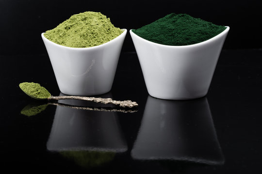 An isolated tablespoon of dried organic wheat grass and spirulina powder, on white rustic background