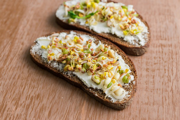 close up of rye bread sandwiches with cream cheese and sprouted mung beans, walnut, sunflower and flax on wooden background. vegan, raw food diet.