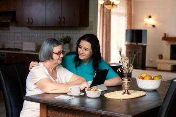 Caring nurse showing a digital tablet to an elderly woman in a nursing home
